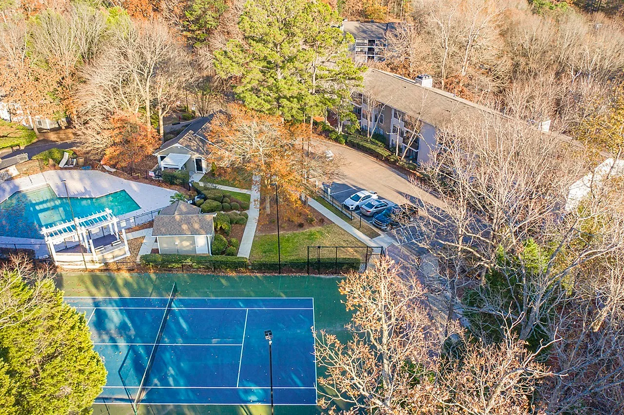 Tennis court with blue surface, pool area with cover, surrounding bare trees and landscaping, Raleigh