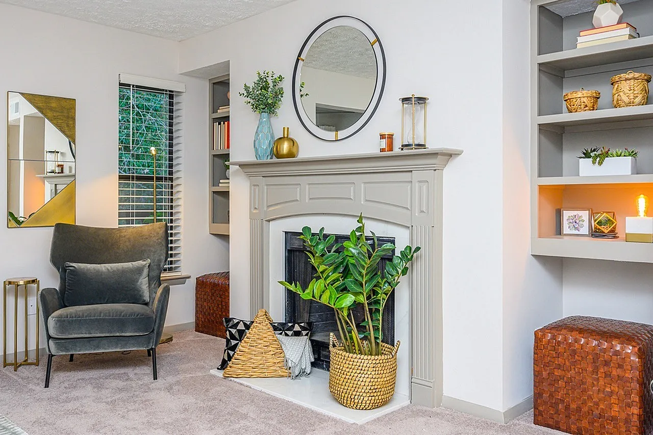 Living room, white fireplace mantel, round mirror, wood-style plank flooring, potted plants