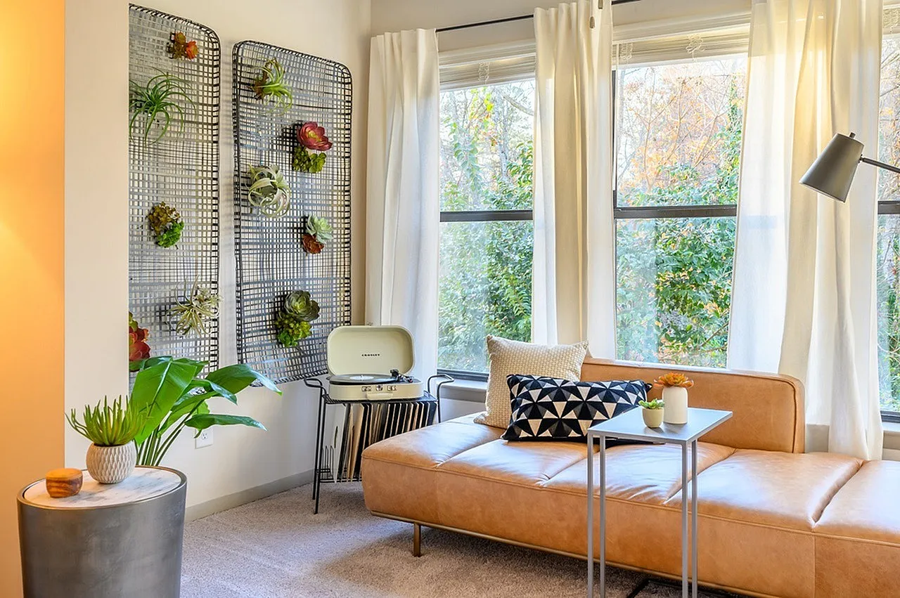 Living room, tan leather sofa, metal frame coffee table, wall-mounted plant grid, large windows