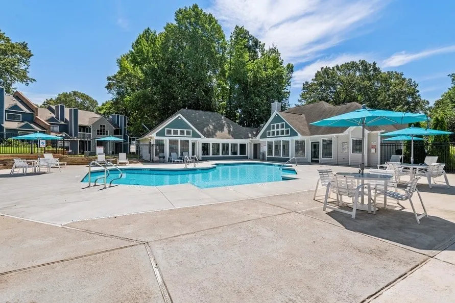Resort-style pool, clubhouse backdrop, lounge seating, umbrella tables