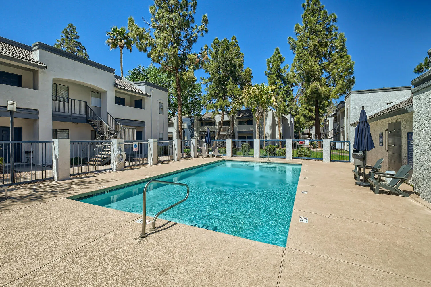 Apartment pool area with palm trees and Adirondack chairs