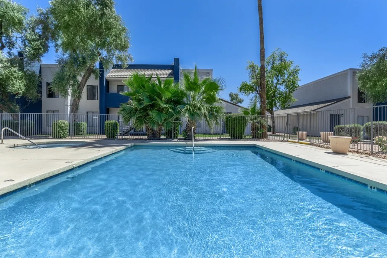 Resort-style pool, clear blue water, palm trees, fenced area, residential buildings