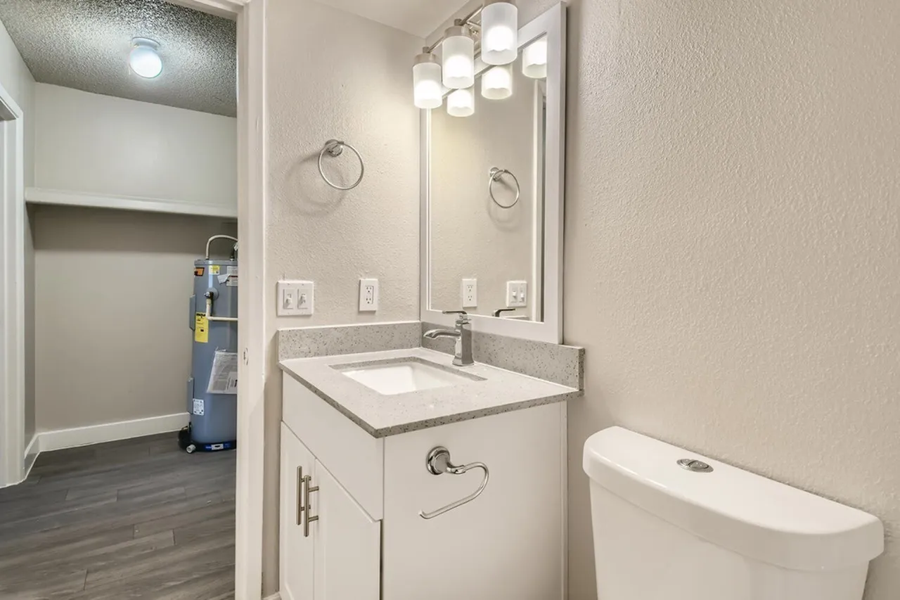 Bathroom, white vanity with quartz countertops, single sink, large mirror with lighting fixtures
