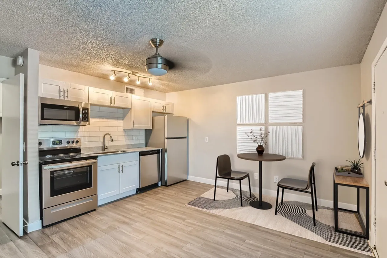 Kitchen with stainless appliances, white cabinetry, backsplash, wood-style plank flooring, dining area with chairs