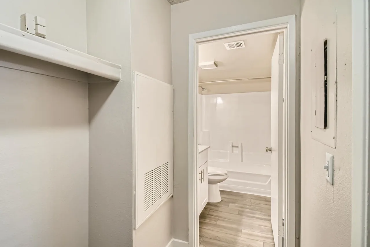Bathroom with toilet, vanity sink, white tile shower surround, wood-style plank flooring, laundry closet access