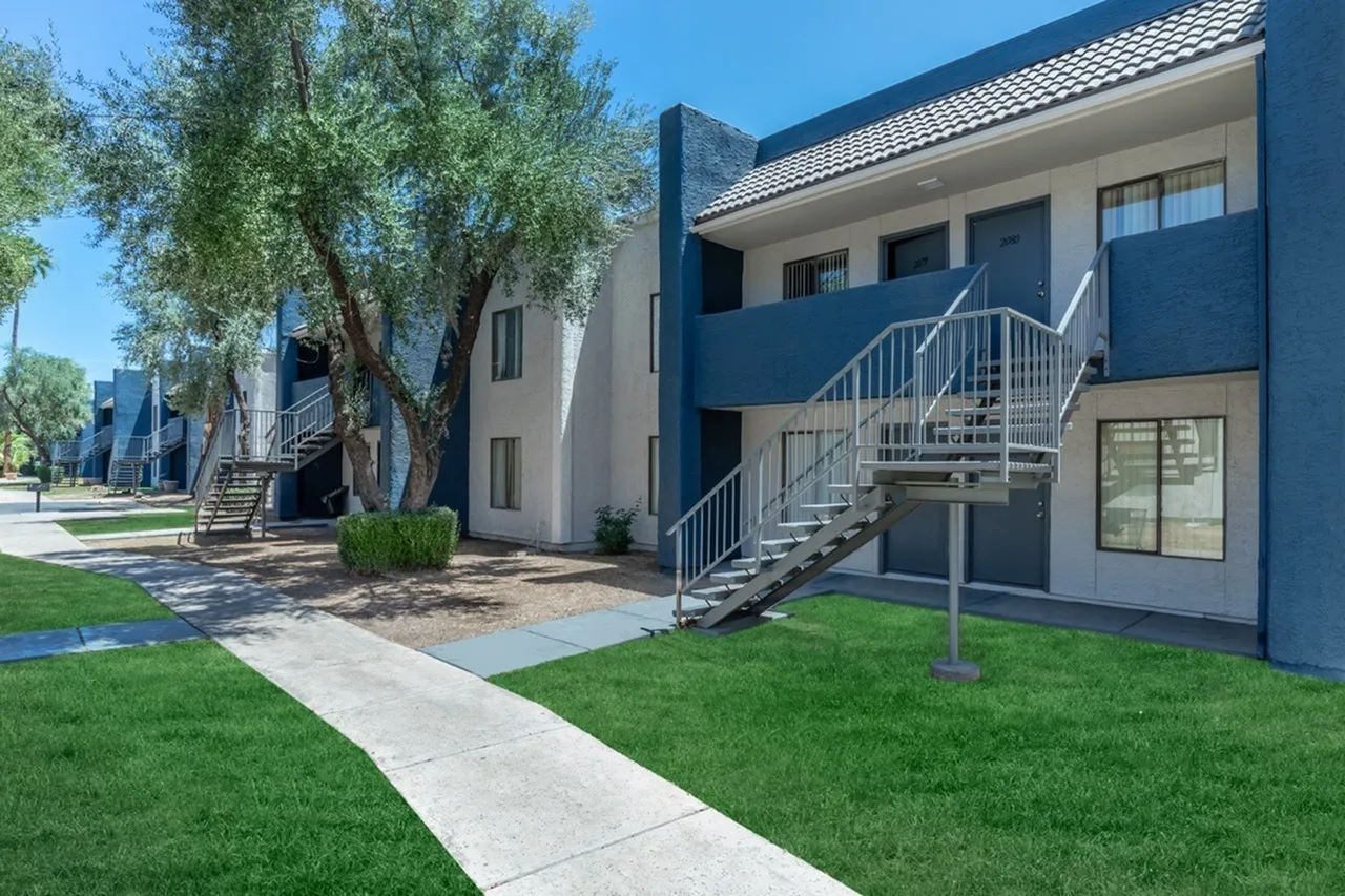 Multistory residential buildings, blue and gray facade, metal staircases, concrete pathways, mature tree, manicured lawn