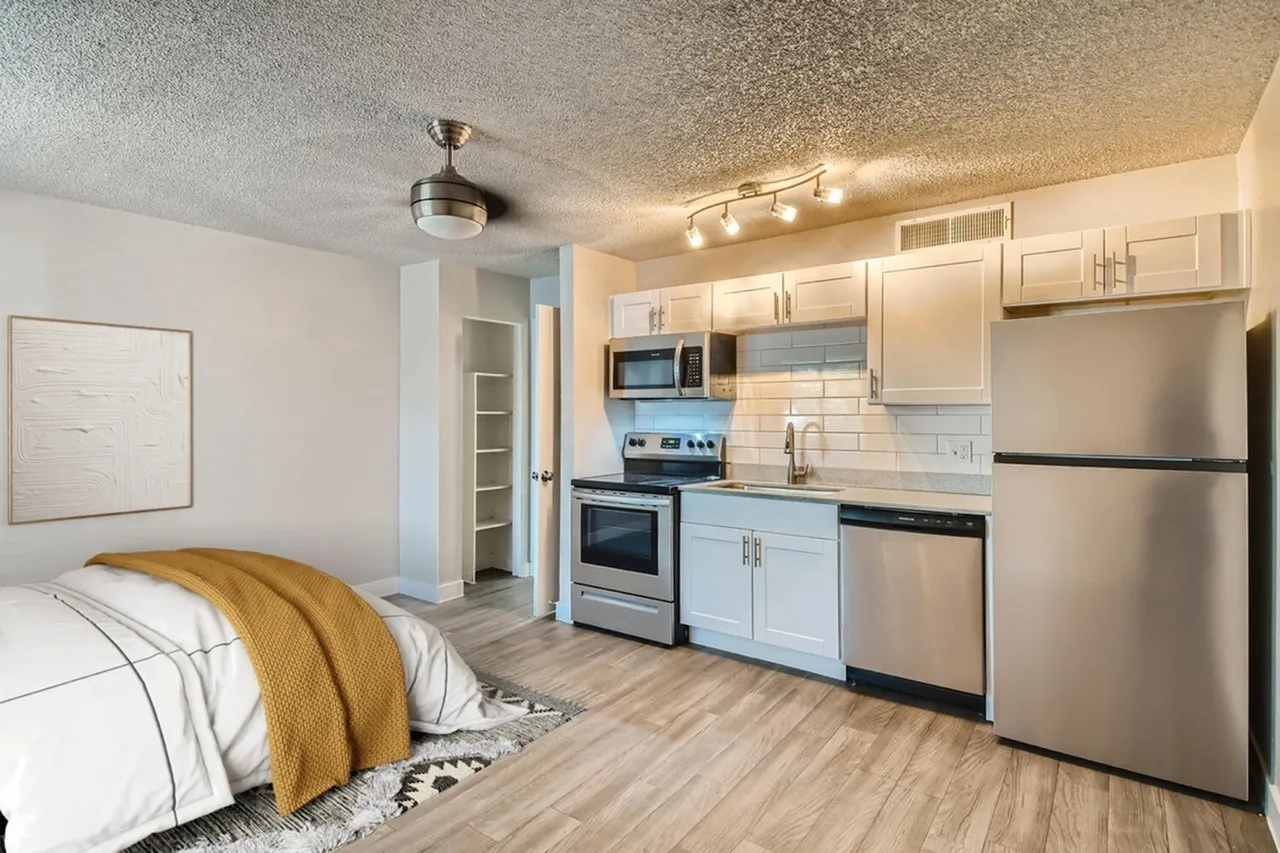 Studio with bed, wood-style plank flooring, white shaker cabinetry, stainless appliances