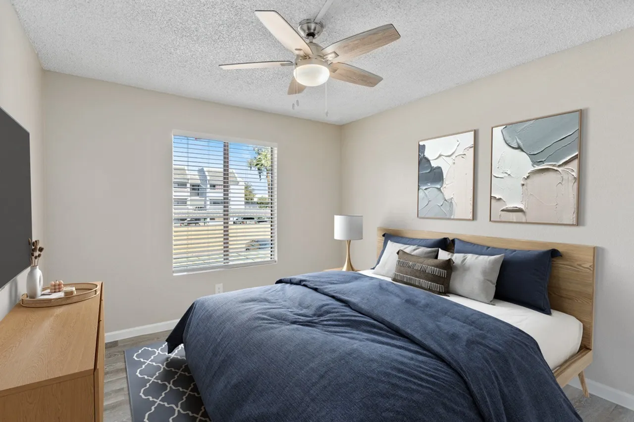 Primary bedroom, blue comforter, wood-style plank flooring, ceiling fan with light