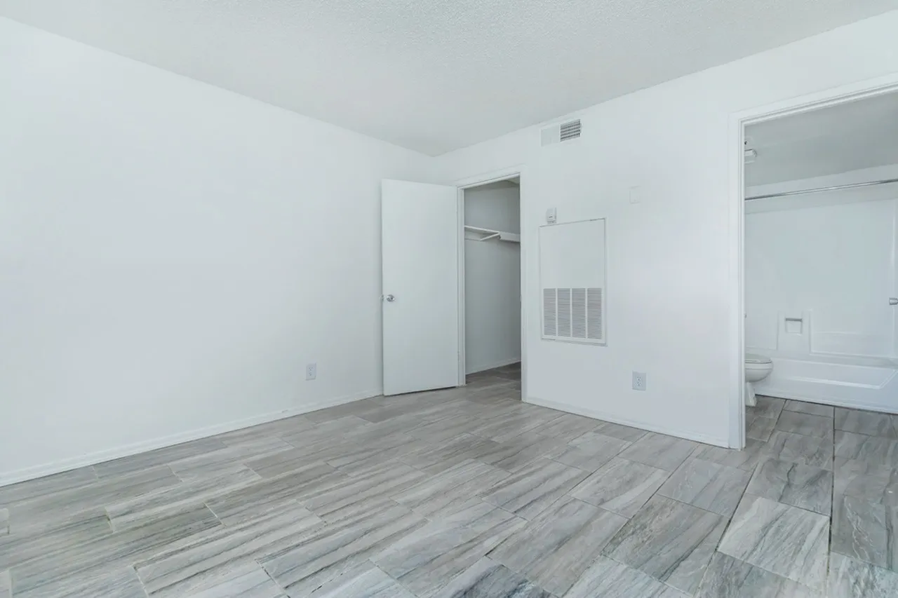 Bedroom, wood-style plank flooring, white walls, closet entry, bathroom view