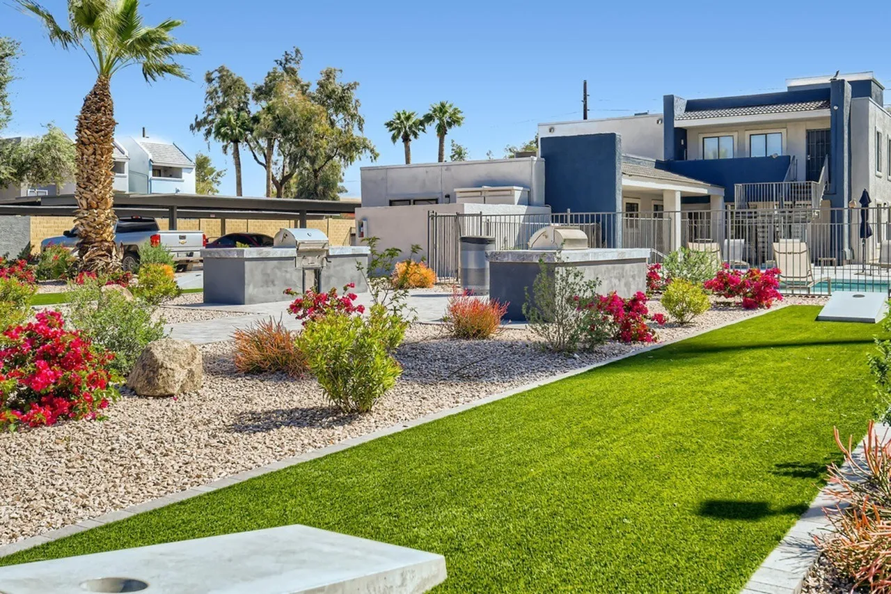 Community courtyard with manicured lawn, desert landscaping, flowering plants, modern residential buildings, pool area