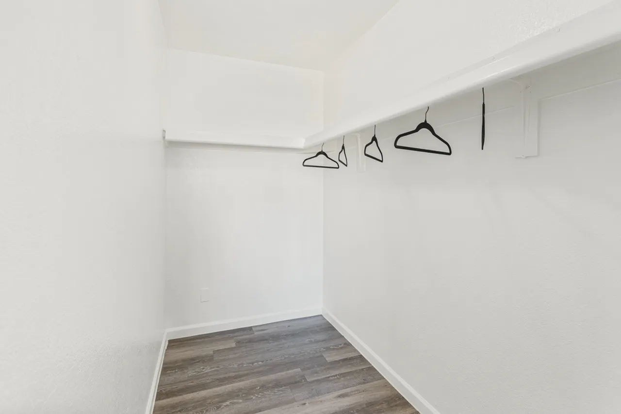 Walk-in closet with white walls, wood-style plank flooring, metal clothing rod and hangers