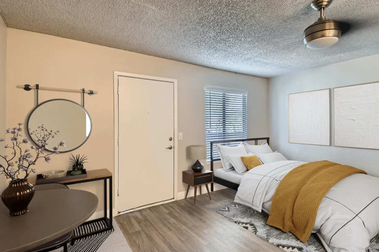 Primary bedroom with wood-style plank flooring, round mirror, bed with yellow throw blanket, vanity desk