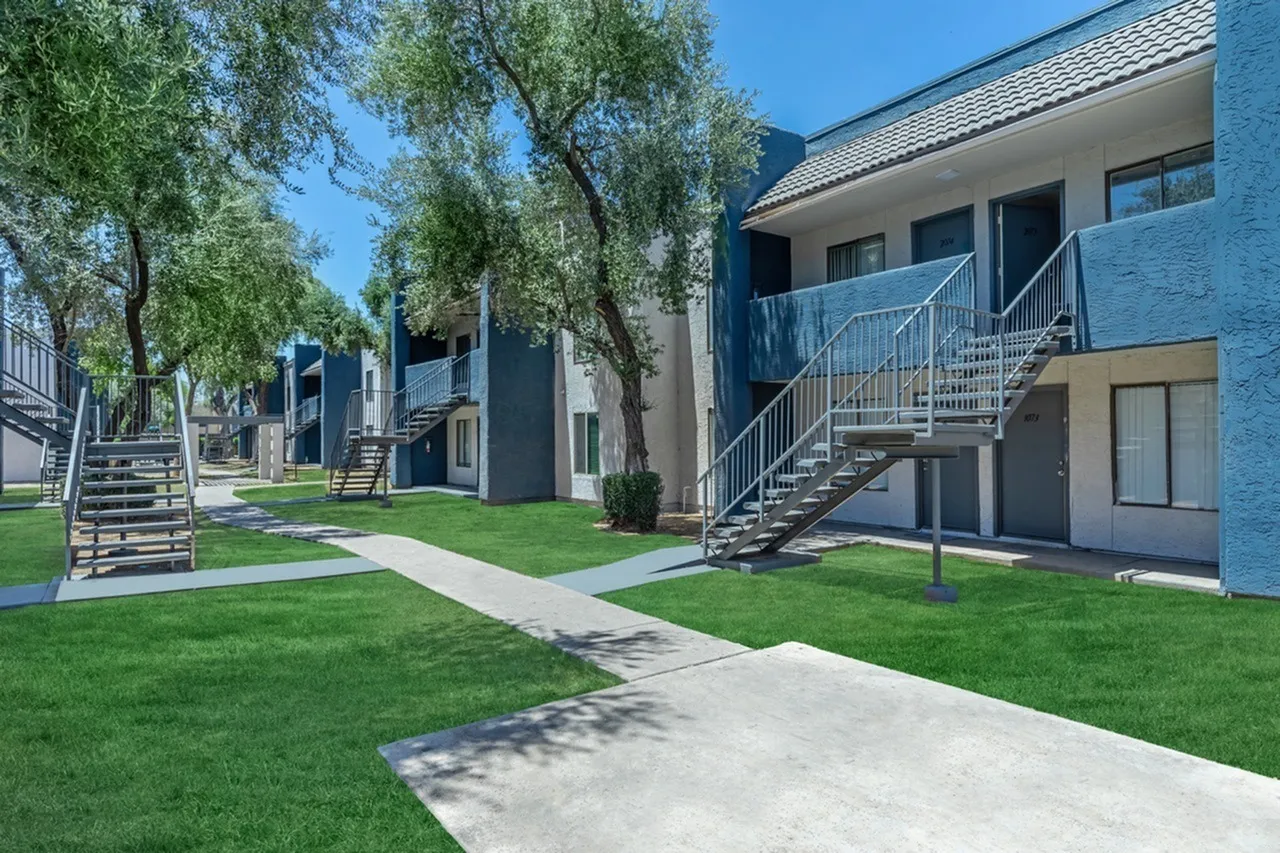 Apartment courtyard, green lawn, metal stair railings, multi-story blue buildings, mature trees