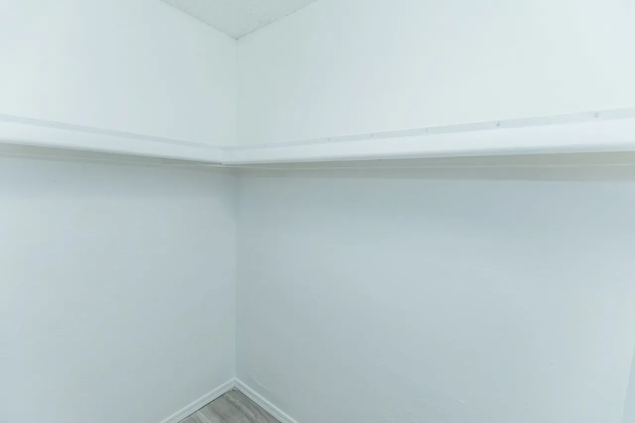 Empty bedroom corner, white drywall, recessed ceiling lights, concrete flooring