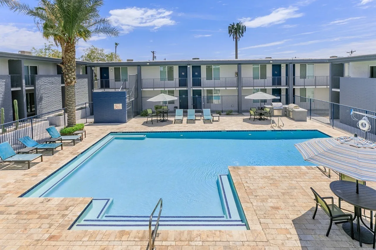 Pool area, blue sparkling water, concrete decking, lounge seating, modern apartment buildings, palm trees, blue sky