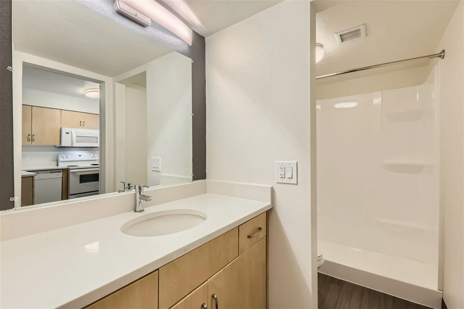 Primary bathroom, wood-style vanity cabinetry, white quartz countertop, chrome faucet, glass shower enclosure