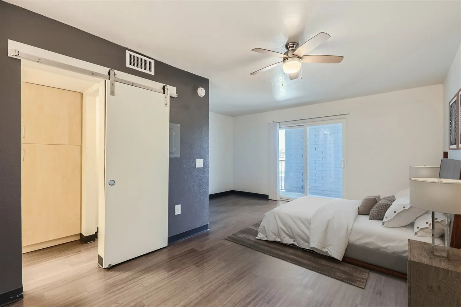 Primary bedroom, wood-style plank flooring, ceiling fan, glass doors to balcony