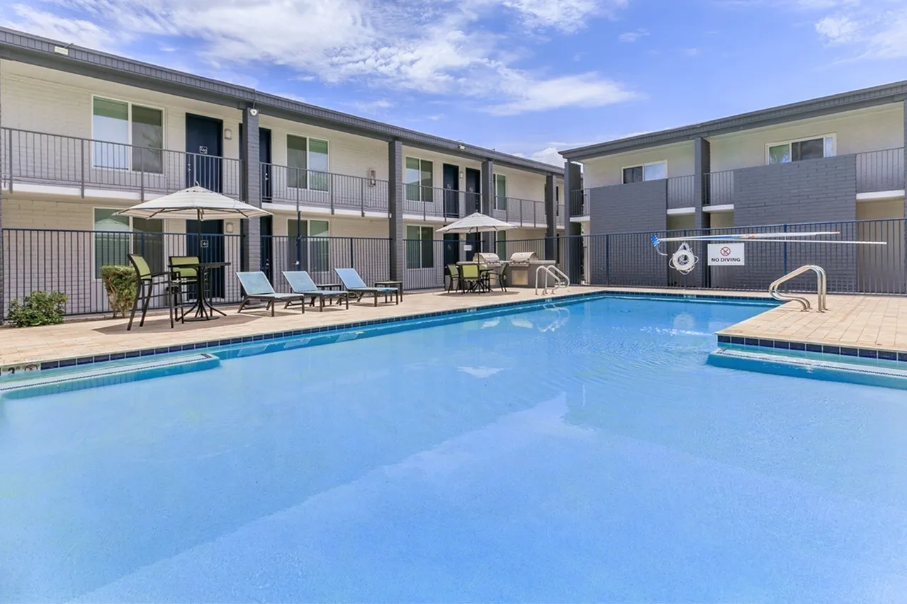 Resort-style pool, lounge seating, apartment buildings, metal fencing