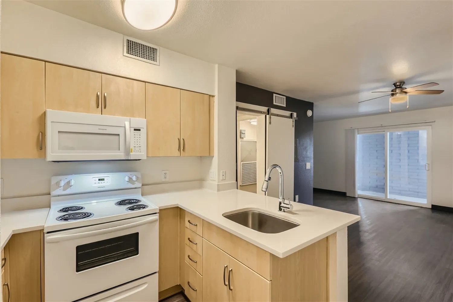 Kitchen with light wood cabinetry, white appliances, white countertops, island sink, wood-style plank flooring in living area