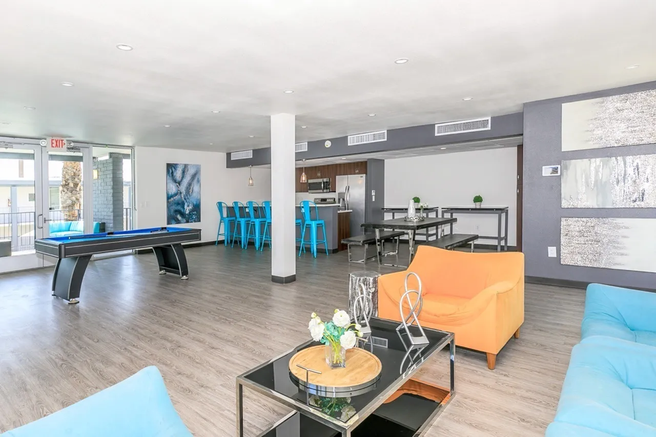 Community lounge, wood-style plank flooring, blue upholstered seating, ping pong table, accent wall