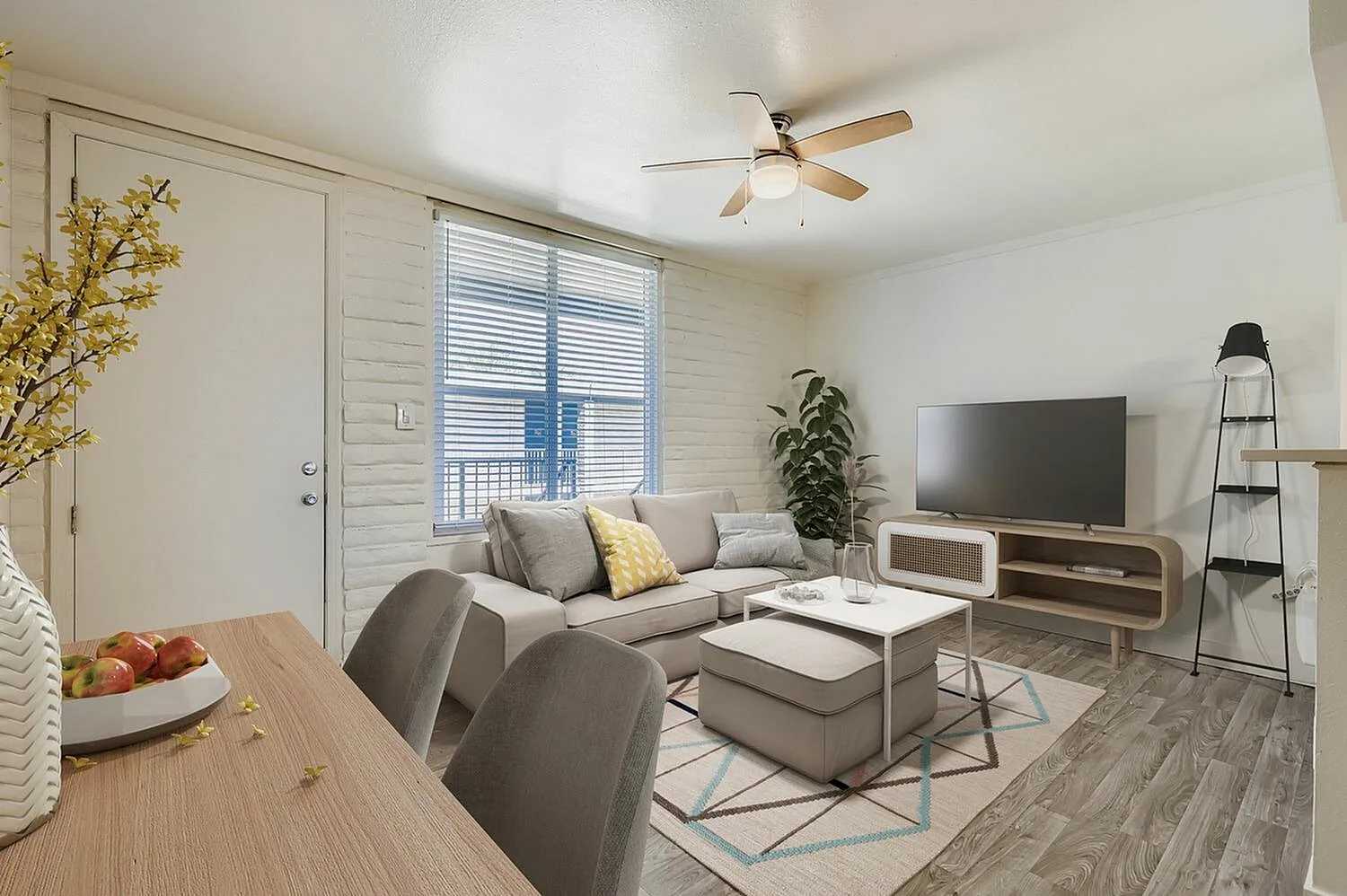 Living room with wood-style plank flooring, gray sofa, flat-screen TV, ceiling fan, entry door