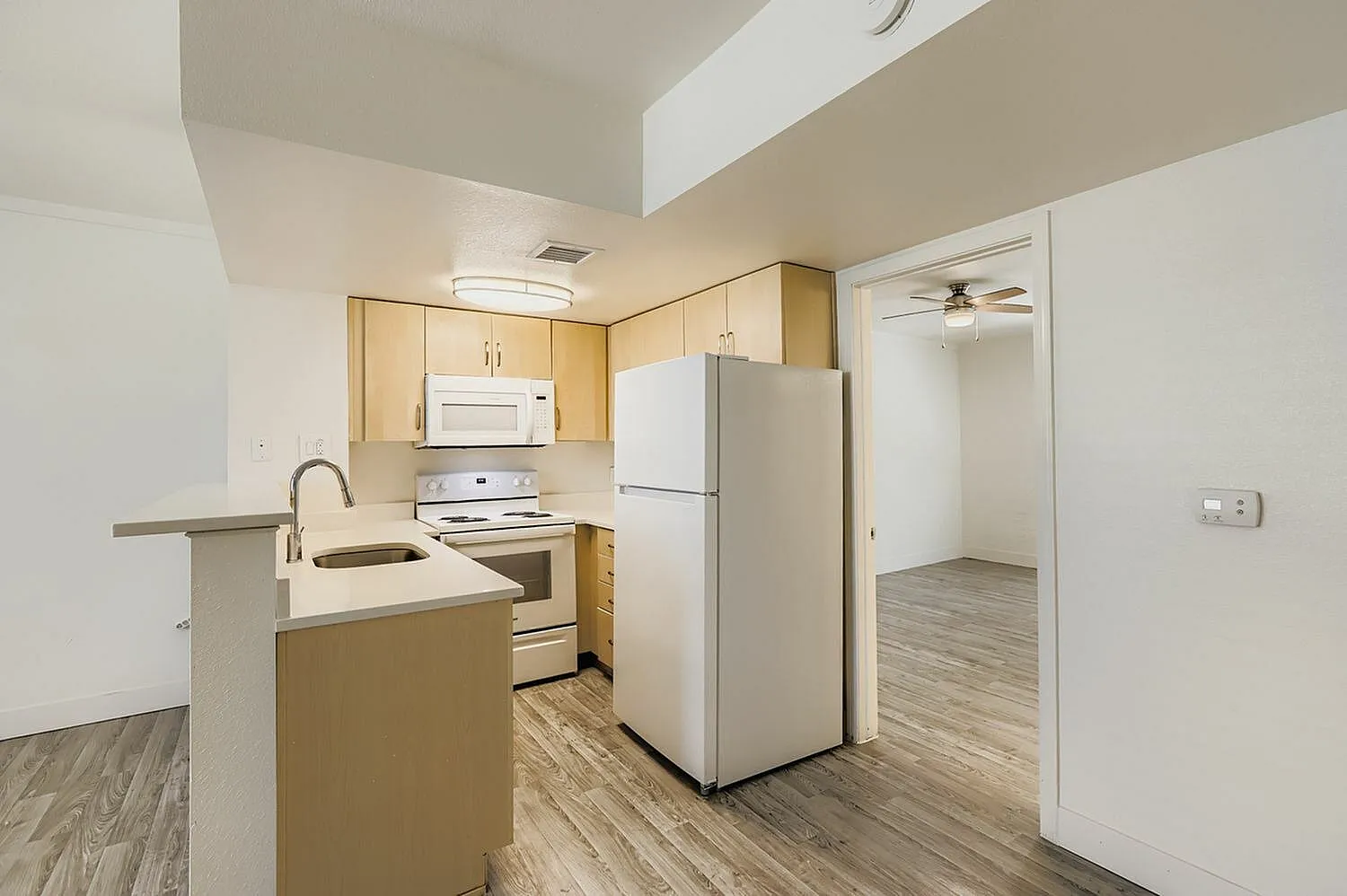 Kitchen, light wood cabinetry, stainless sink, white appliances, wood-style plank flooring