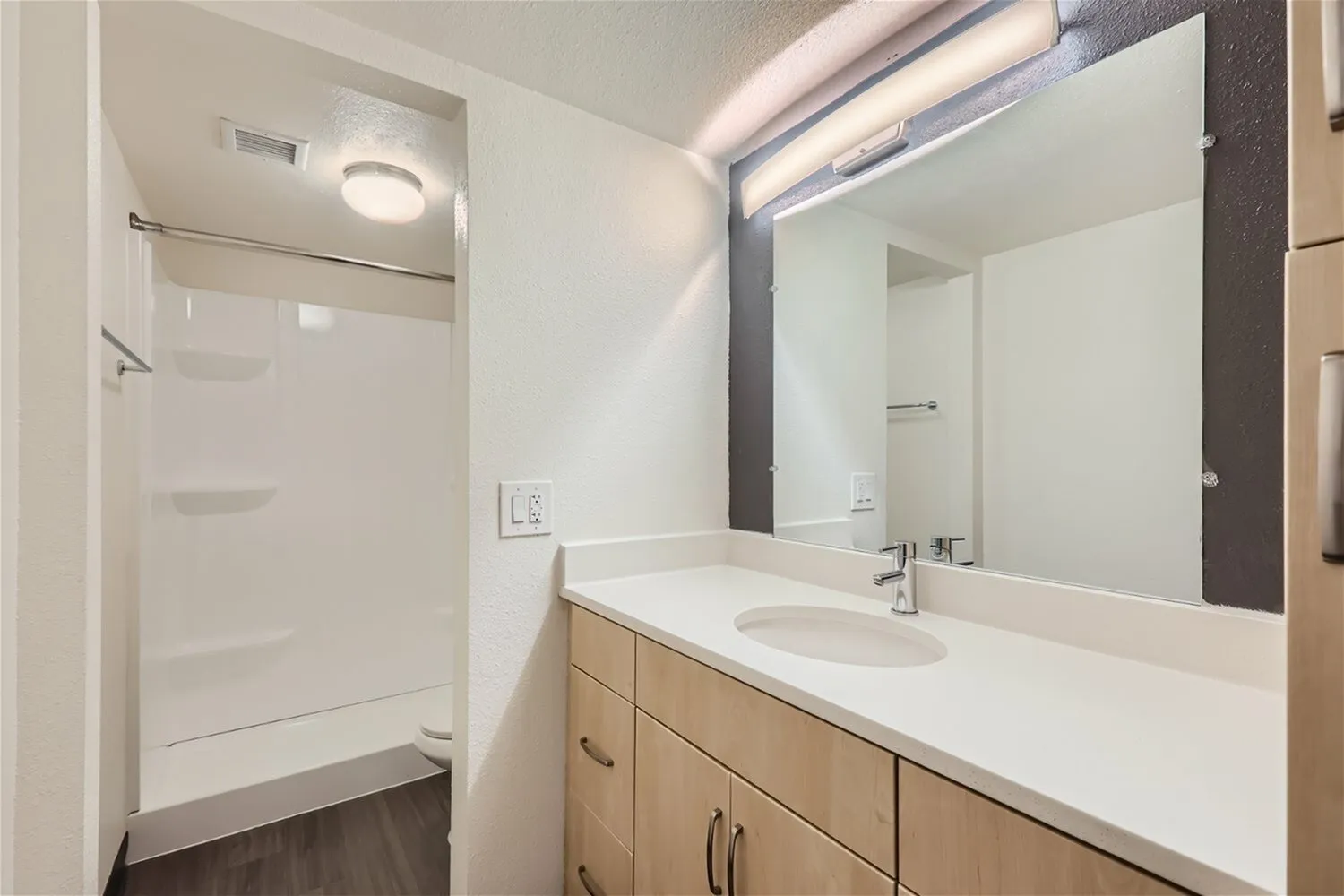 Primary bathroom, wood-style vanity cabinetry, white quartz countertops, walk-in shower