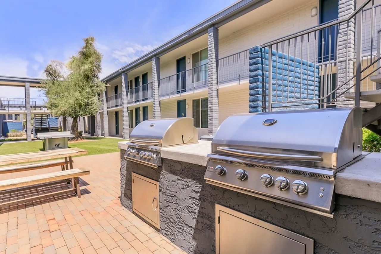 Patio grilling area, stainless steel built-in grills, stone accents, wood-style plank flooring, modern apartment building