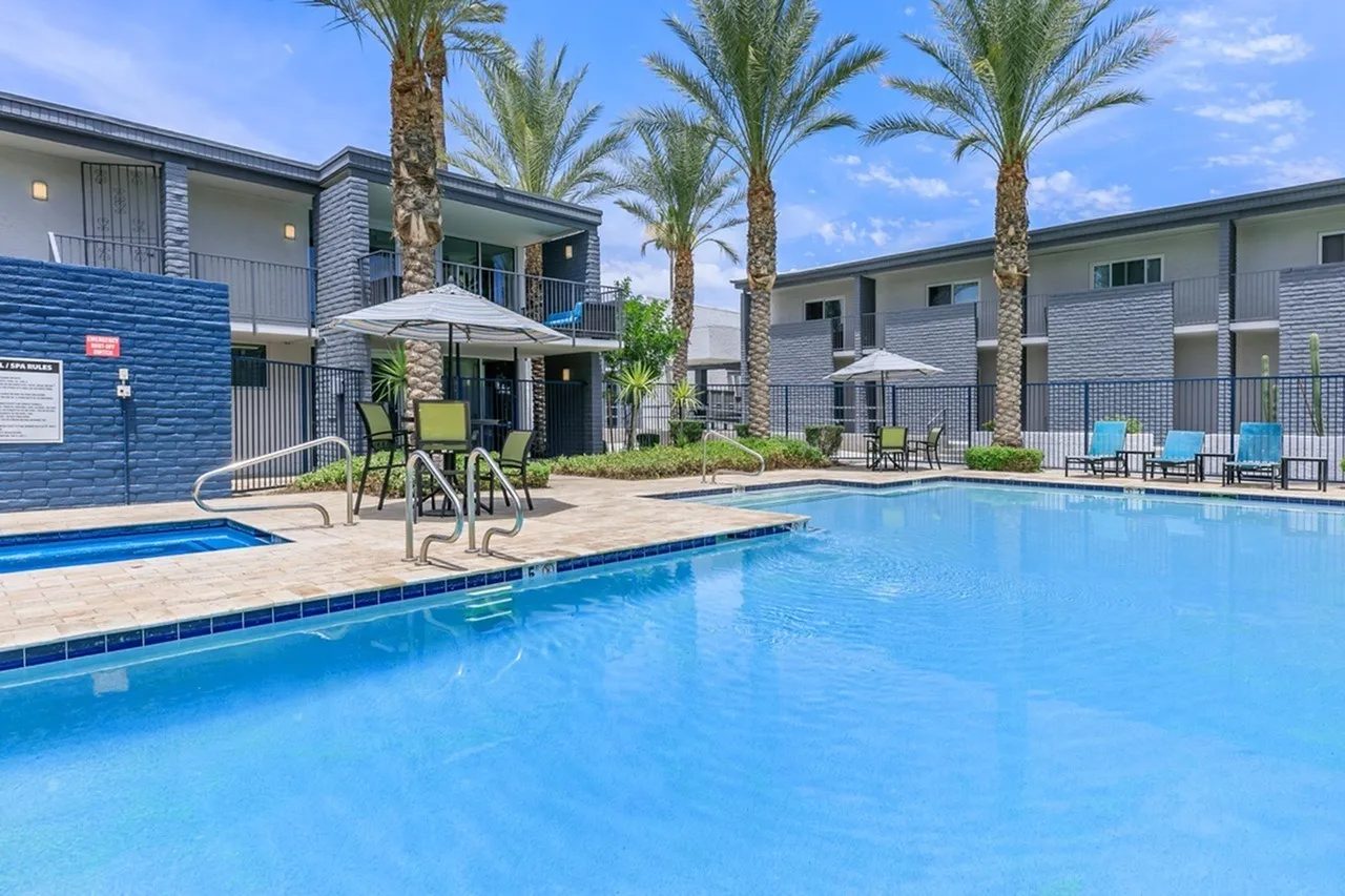 Swimming pool with lounge chairs, umbrellas, palm trees, modern apartment buildings
