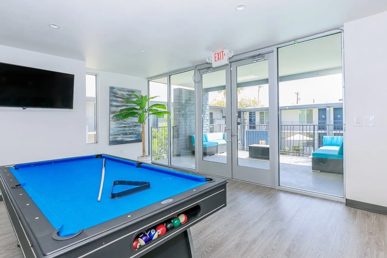 Game room, blue billiards table, wall-mounted TV, wood-style plank flooring, glass doors to balcony