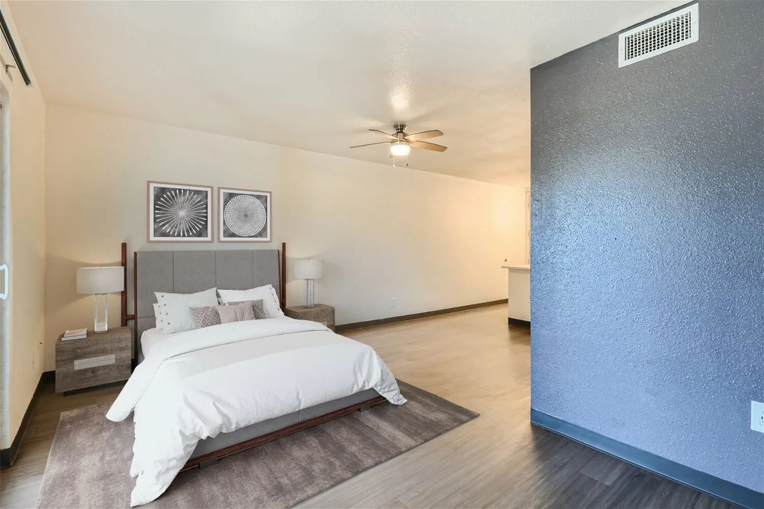 Primary bedroom, gray upholstered headboard, wood-style plank flooring, ceiling fan, two-tone walls