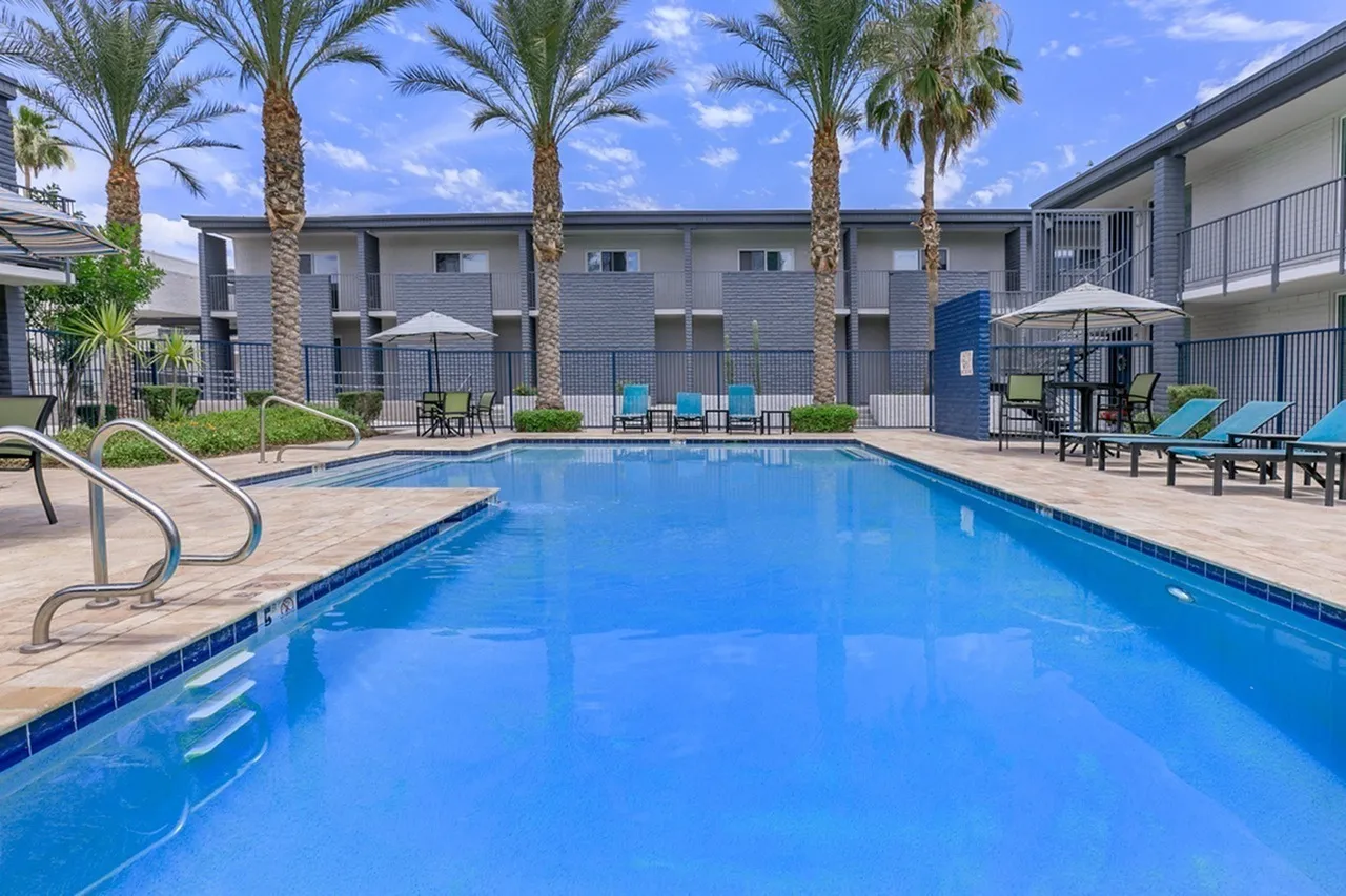 Swimming pool with lounge seating, palm trees, residential building, clear sky