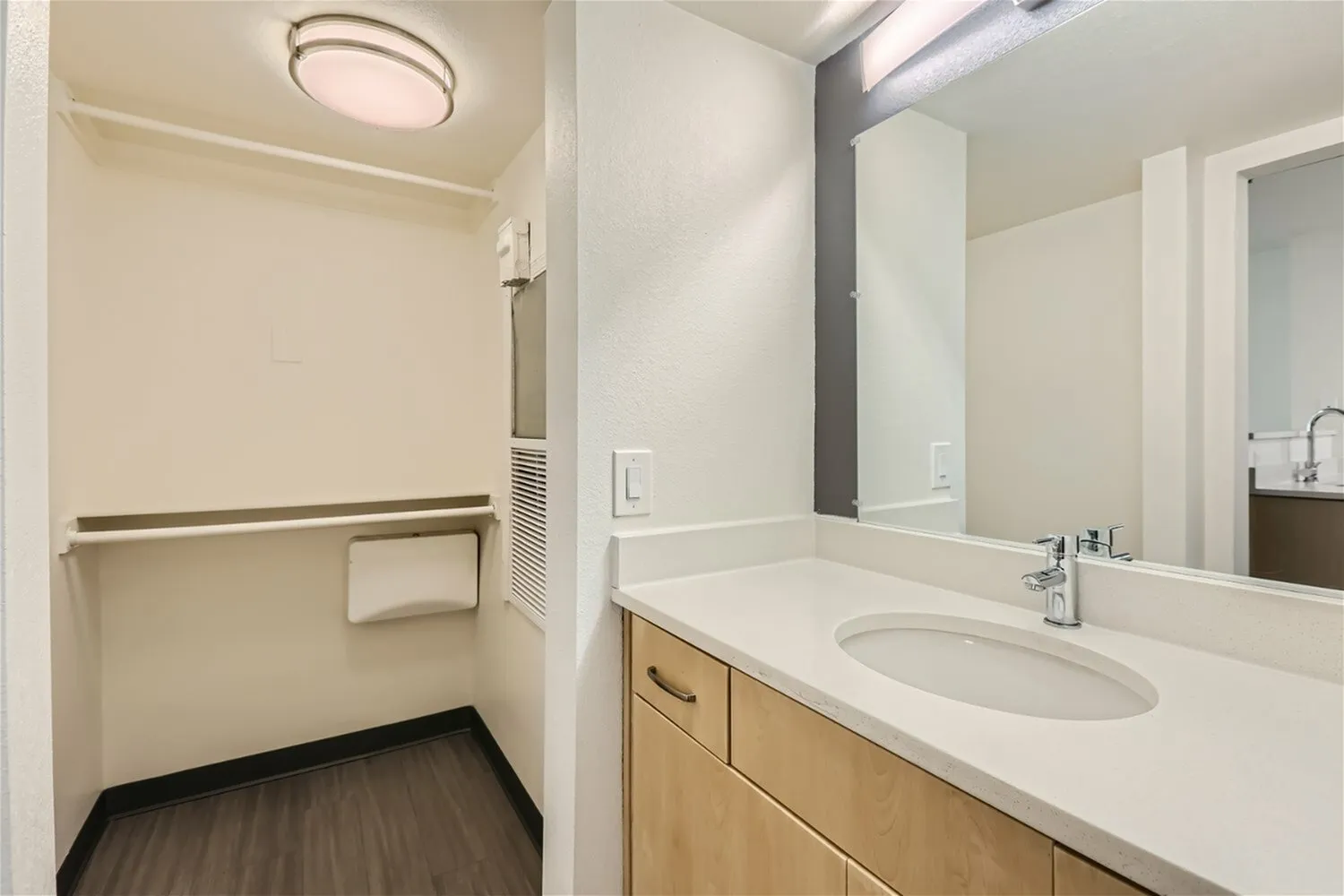 Bathroom vanity with white quartz countertops and wood-style cabinetry, large mirror, chrome faucet, walk-in closet with wood-style plank flooring