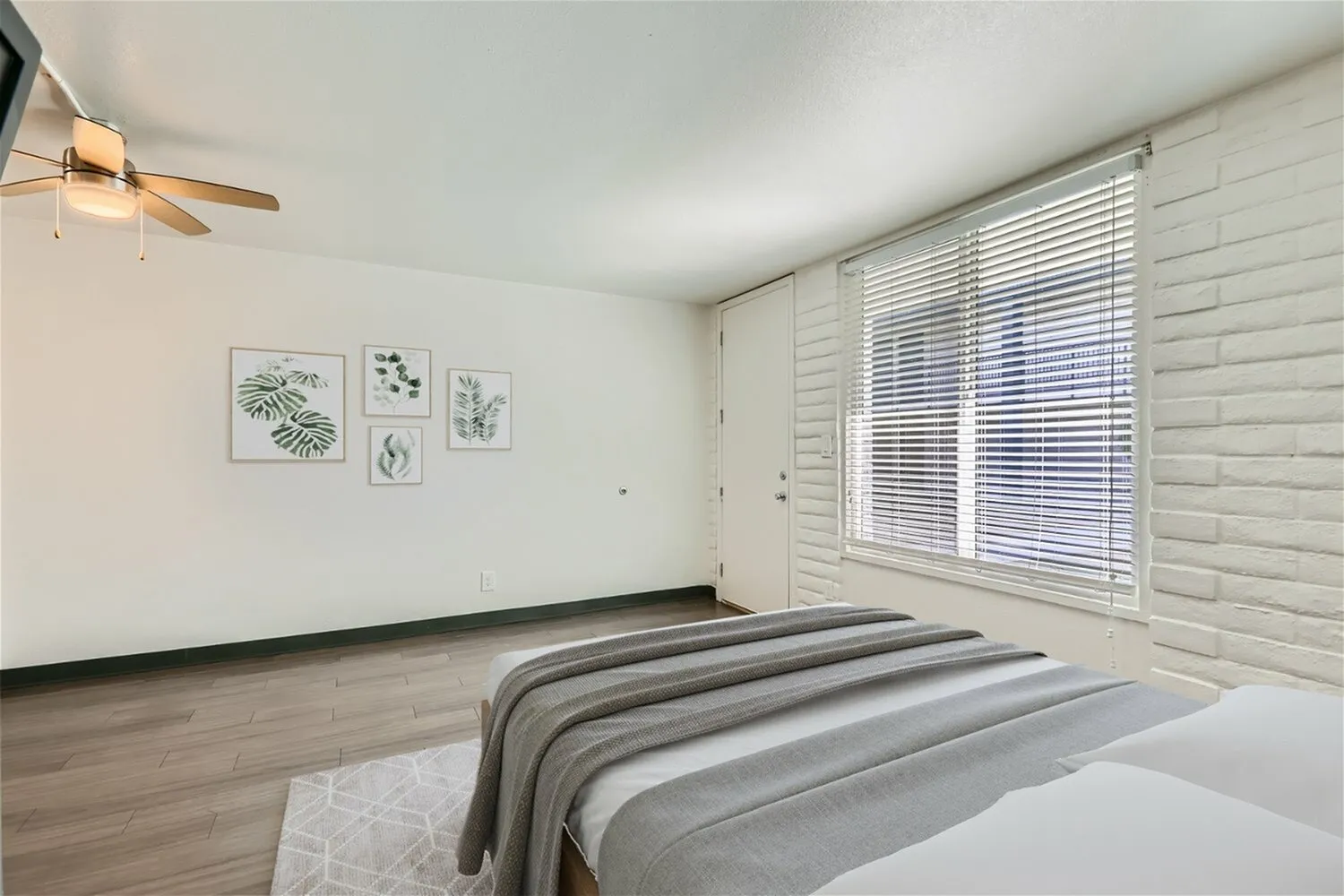 Primary bedroom, wood-style plank flooring, white shutter blinds, ceiling fan, botanical wall art
