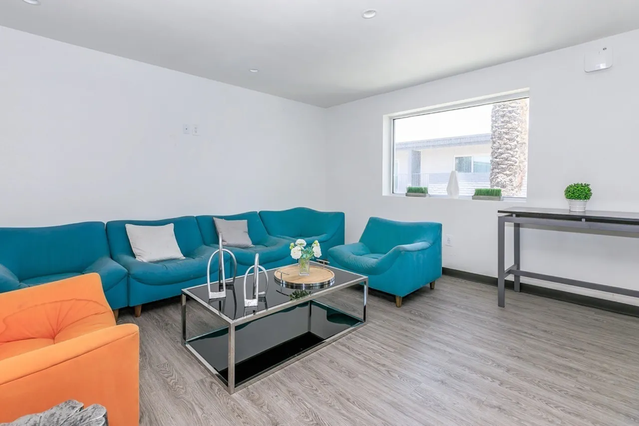 Living room, teal sofa, orange accent chair, wood-style plank flooring, glass coffee table