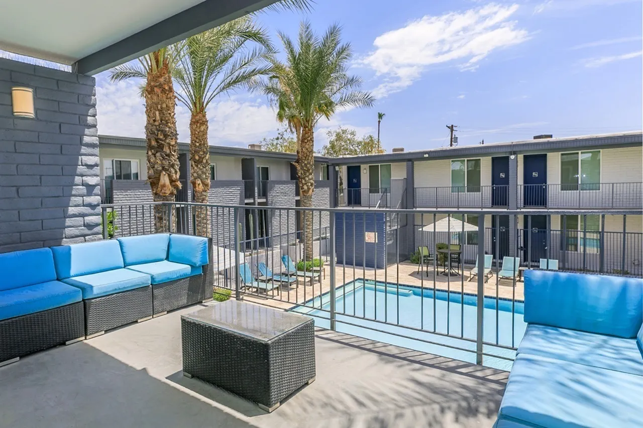Pool deck with blue cushioned seating, metal railing, palm trees, residential buildings