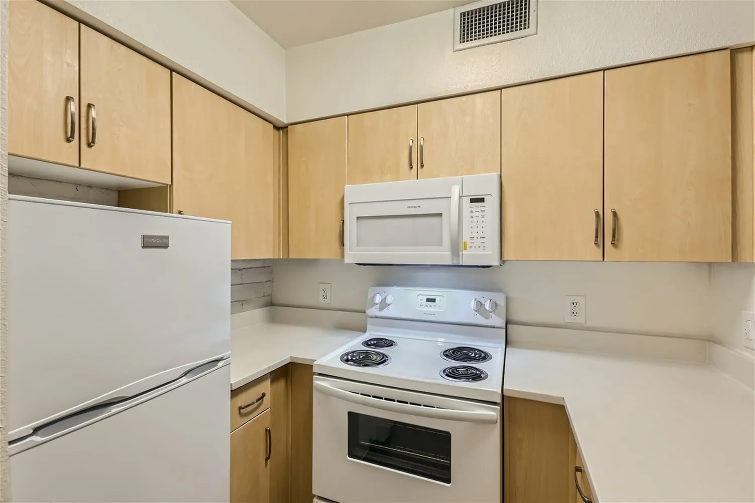 Kitchen, light wood cabinetry, white appliances, beige countertops, microwave above range