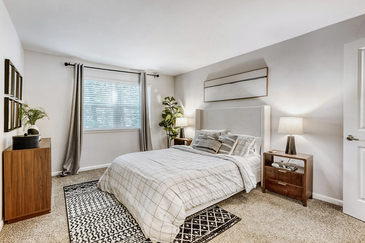 Primary bedroom, gray upholstered headboard, wood nightstands, area rug, window with gray curtains