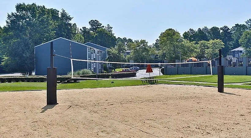 Outdoor sand volleyball court with net, brown steel posts, blue building, green lawn, trees