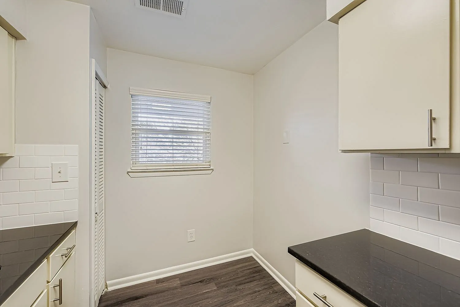 Galley kitchen, white subway tile backsplash, black countertops, white cabinetry, wood-style plank flooring