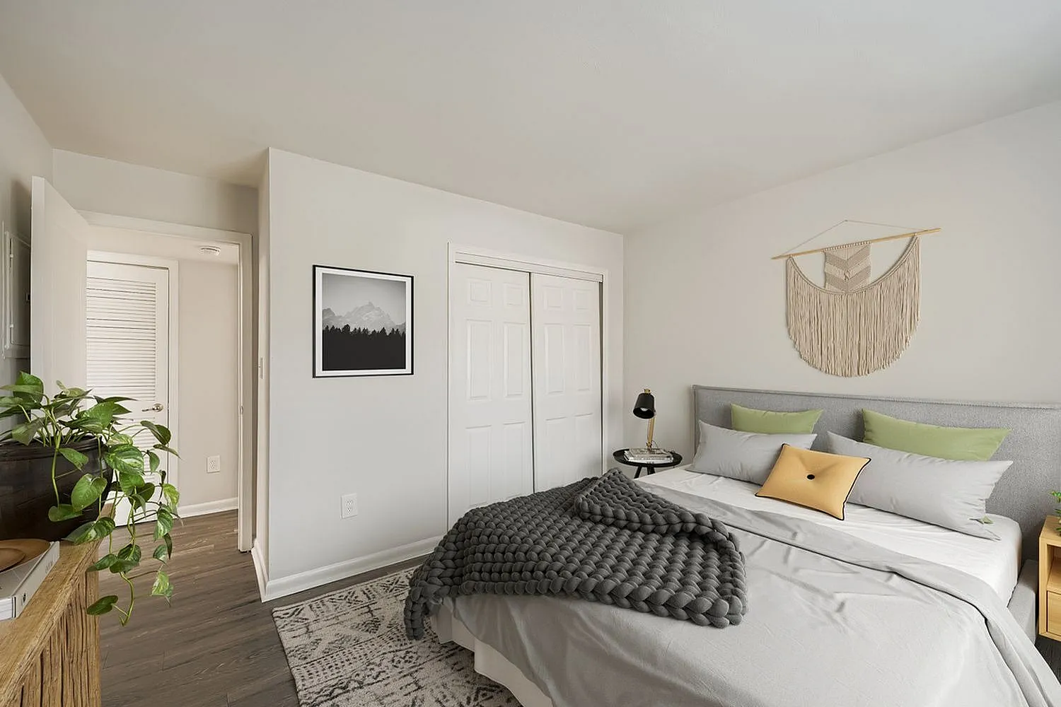 Primary bedroom, gray upholstered headboard, wood-style plank flooring, macramé wall hanging