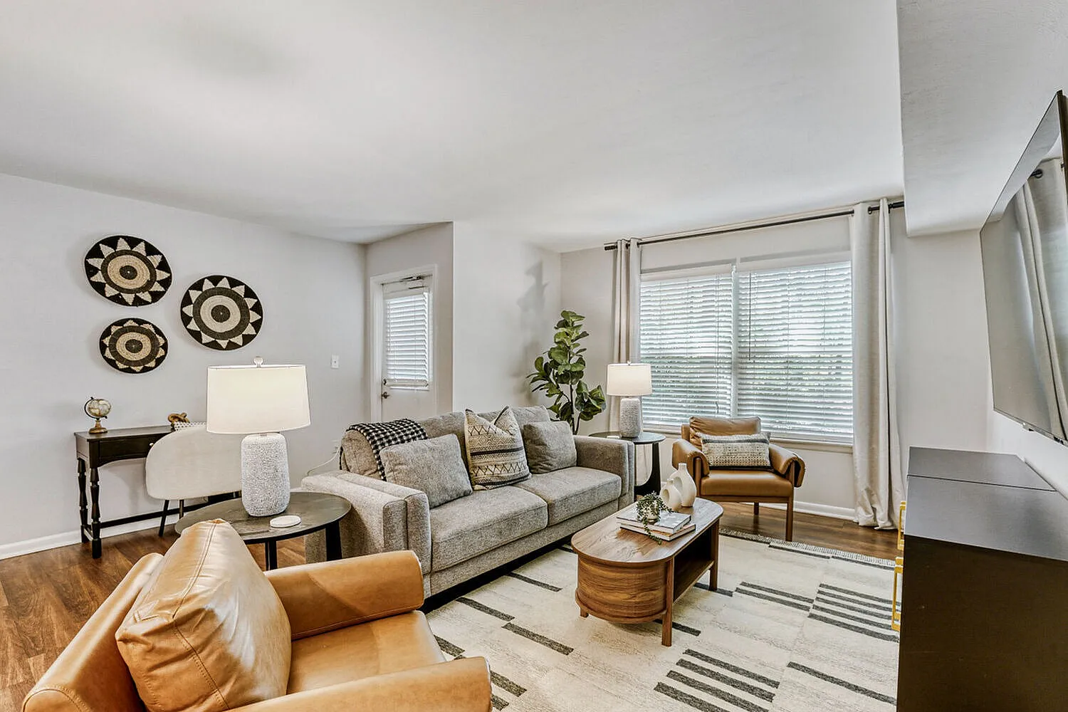 Living room, wood-style plank flooring, gray upholstered sofa, cognac leather chair, decorative wall plates