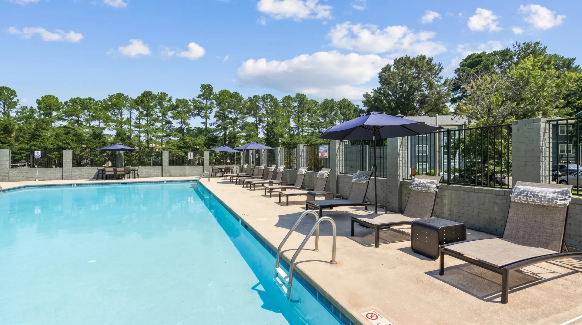 Resort-style swimming pool, lounge chairs, dining area, shade umbrellas, tree line