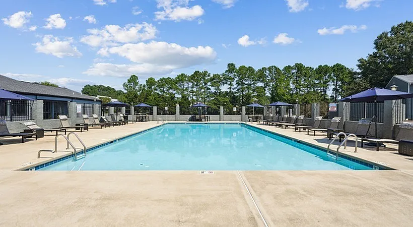 Community swimming pool, concrete deck, lounge seating, residential buildings, tree line