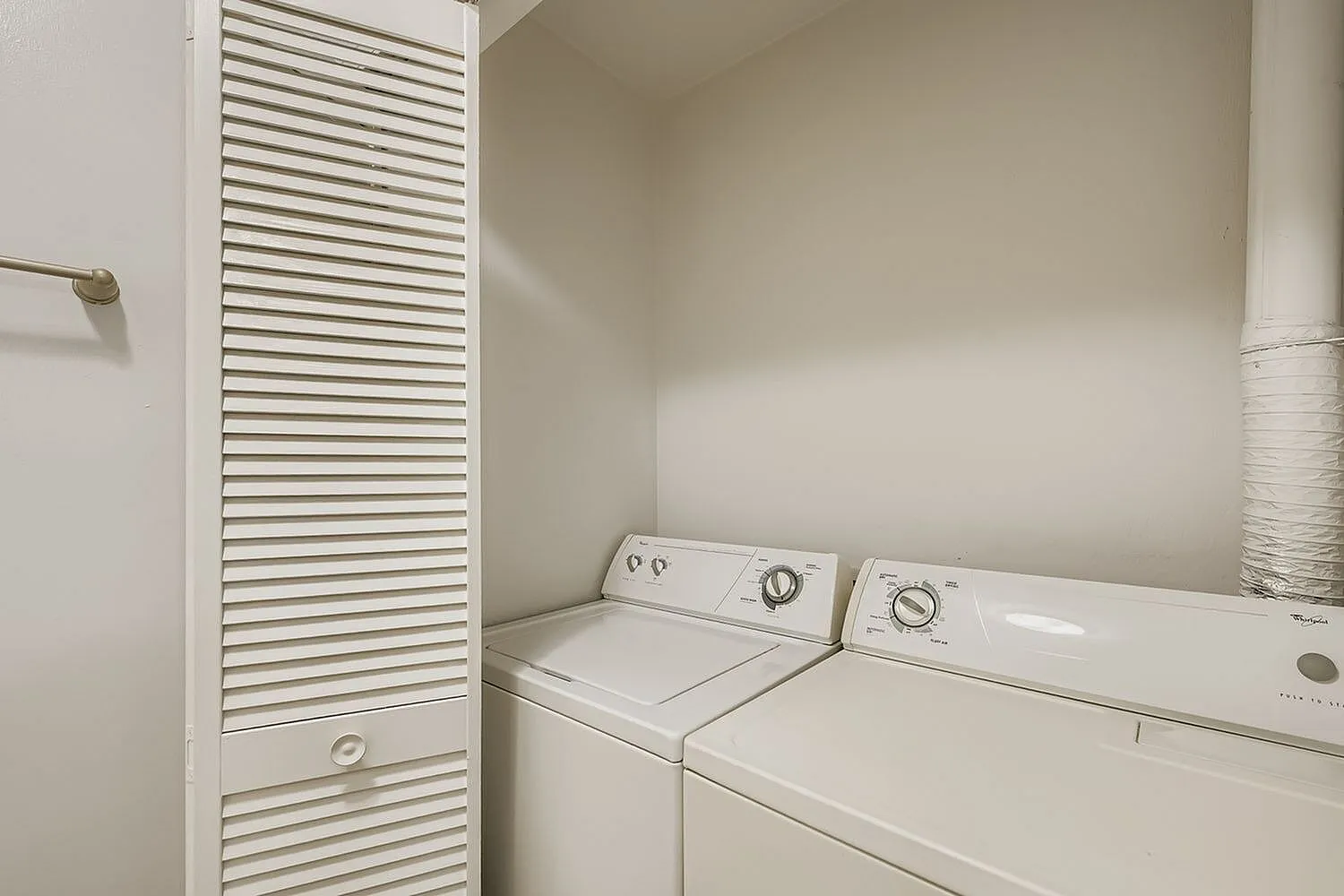 Laundry room, white stacked washer and dryer, louvered storage door, neutral walls