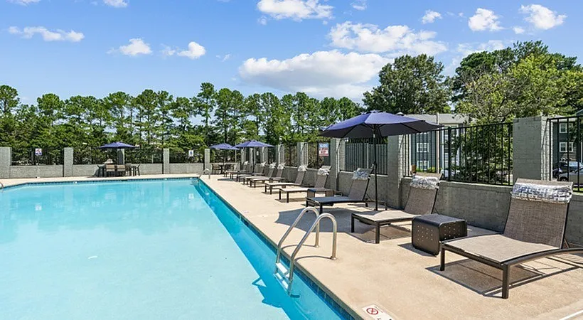 Resort-style swimming pool, lounge chairs, dining area, shade umbrellas, tree line