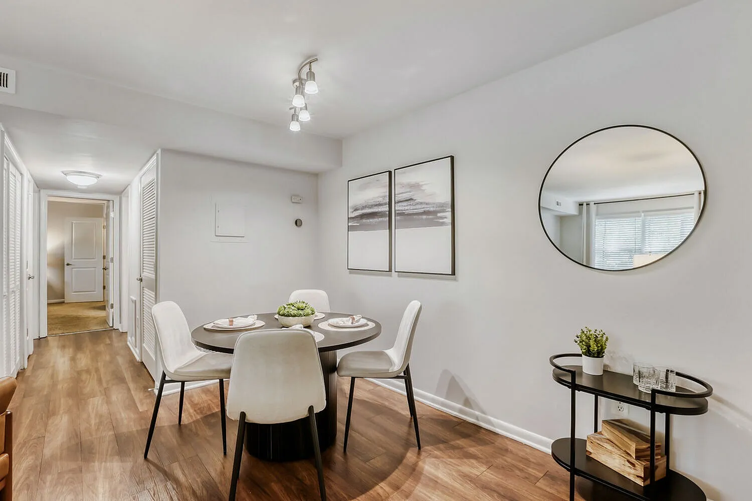 Dining room, round table with cream chairs, wood-style plank flooring, round mirror, framed artwork