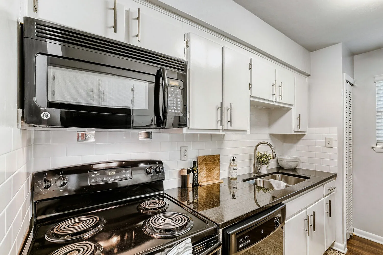 Kitchen, white cabinetry, black electric range, microwave hood, quartz countertops