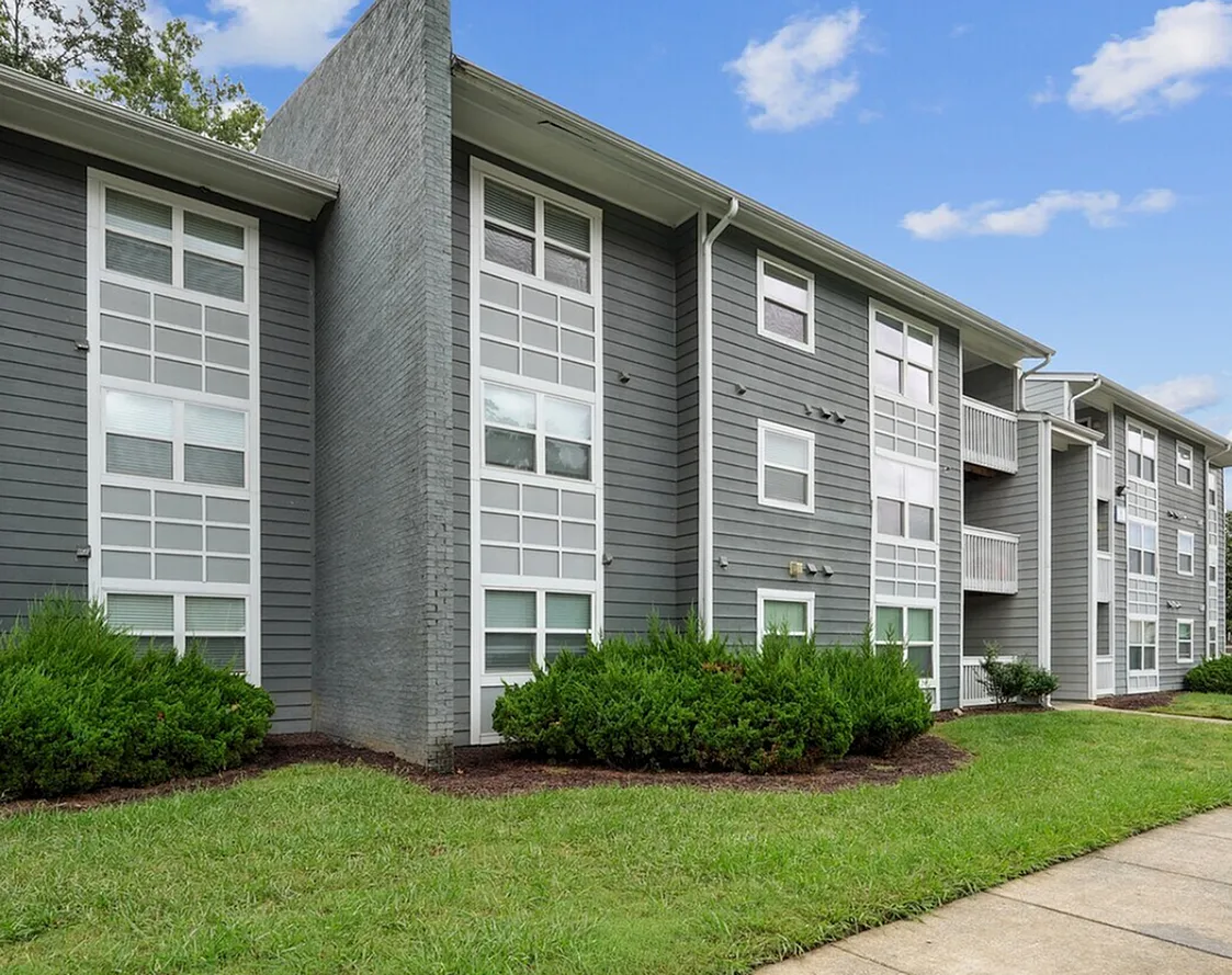 Apartment building, gray siding, white frame windows, landscaped grounds, blue sky