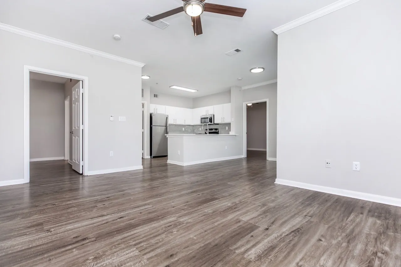 Open living and kitchen area, wood-style plank flooring, white cabinetry, stainless appliances, ceiling fan